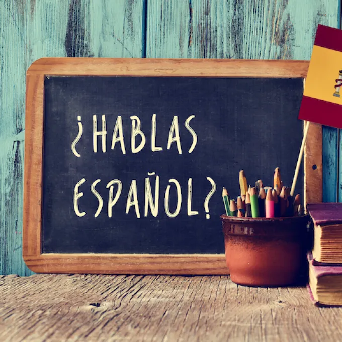 "hablas espanol written on small black chalkboard with flag next to it"